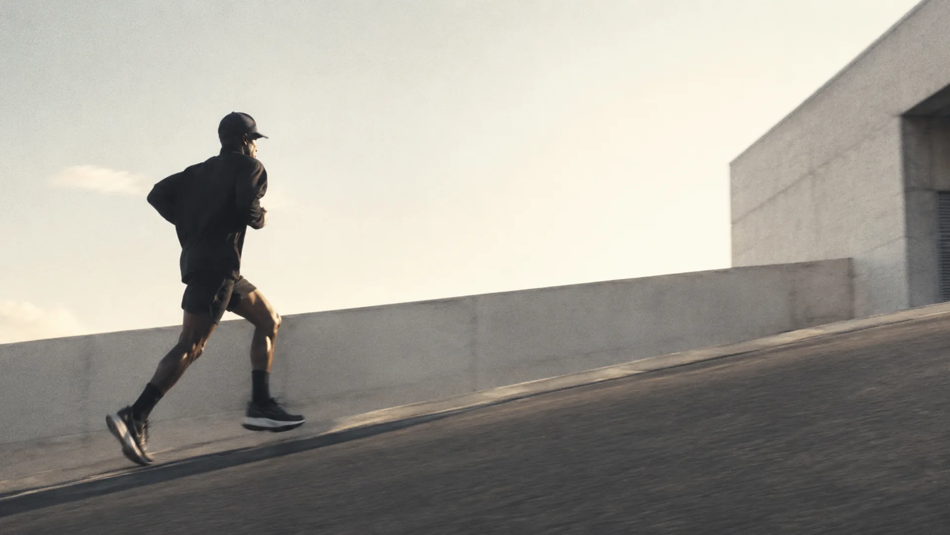 Wide editorial mood image of a runner moving along a concrete ramp in early light.