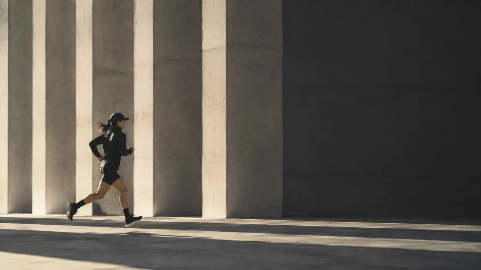 A runner passing tall pale concrete columns in dry, low afternoon light.